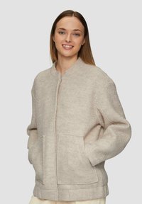 Beige wolmix jas met een ronde kraag, rits aan de voorkant en twee voorzakken. Ontspannen pasvorm met een gestructureerde afwerking.