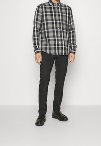 Černá a šedá kostičkovaná košile na knoflíky, zkombinovaná s černými kalhotami a černými koženými botami, která předvádí klasický střih a strukturovaný design.