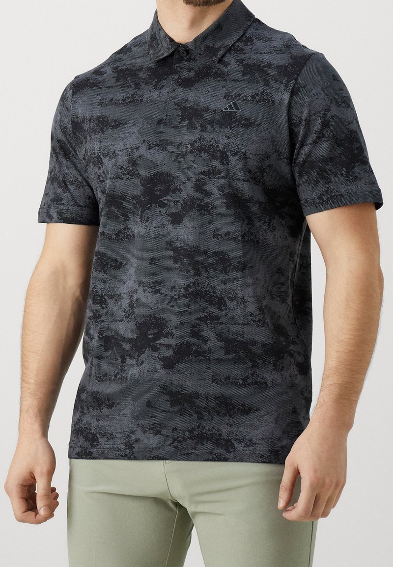 Černé polo tričko s texturovaným, abstraktním vzorem. Má límečkový výstřih a krátké rukávy, vyrobené z prodyšného materiálu.