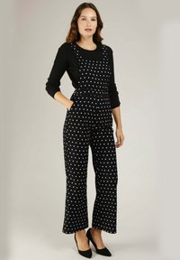 Salopette noire à pois avec un bavoir ajusté, un design à jambes larges et des poches. Le haut est composé d'un t-shirt à manches longues noir à côtes.