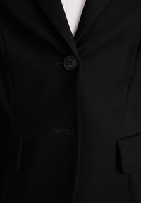 Zwarte blazer met een enkele knoopsluiting, gesneden revers en twee voorzakken. Glad materiaal met een getailleerde pasvorm.