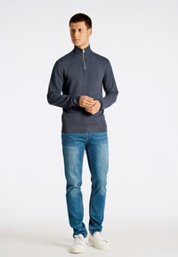 Tummansininen vetoketjullinen neule, jossa on pystykaulus, yhdistettynä vaaleansinisiin farkkuihin ja valkoisiin tennareihin. Yksinkertainen muotoilu pehmeällä tekstuurilla.