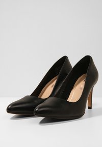 Escarpins en cuir noir avec un bout pointu, une silhouette élancée et un talon aiguille. Texture lisse avec une finition mate.