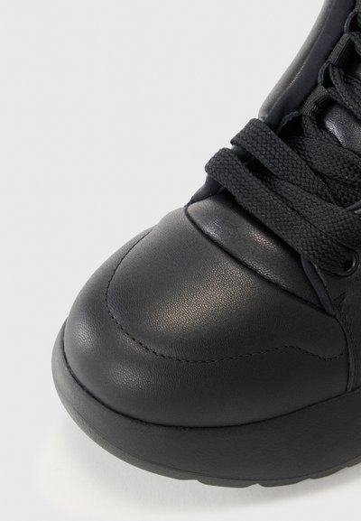 Zwarte sneaker van glad leer, met een ronde neus, gestructureerde veters en een dikke rubberen zool met subtiele stikdetails.