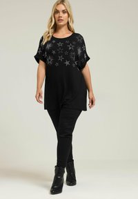 Czarny, krótki rękaw top z srebrnym nadrukiem w gwiazdy, połączony z czarnymi obcisłymi spodniami i botkami, tworząc luźną sylwetkę.