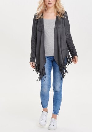 Harmaa nubukkiverhoiltu fringed cardigan, jossa on avoin etuosa, sivutaskut ja teksturoitu pinta, päällä harmaa yläosa ja siniset farkut.