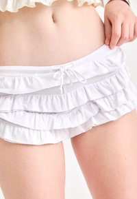 Shorts blancs à volants multiples, avec une taille à cordon de serrage. Le matériau semble doux et léger.
