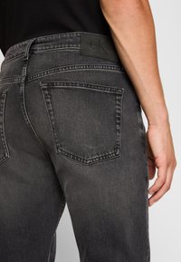 Šedé džíny z denimu s přiléhavým designem. Mezi vlastnosti patří hladká textura, styl pěti kapes a značková kožená nášivka černé barvy na pase.