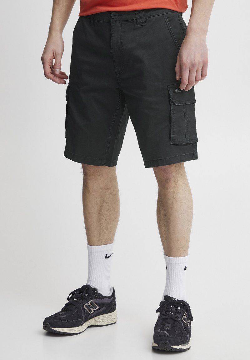 Svarte cargo-shorts laget av bomull, med sidelommer, en avslappet passform og litt over-knelengde, kombinert med svarte sneakers.