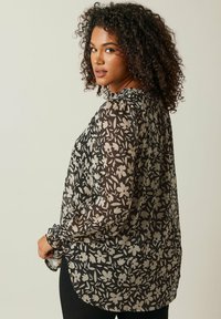 Blusa nera trasparente con motivo floreale grigio chiaro, maniche lunghe con polsini arricciati e vestibilità morbida. Finitura testurizzata.