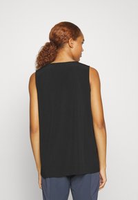 Top preto sem mangas com um corte relaxado, apresentando um decote redondo e detalhes sutis de costura na parte de trás. Textura suave.