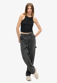 Zwarte, cropped tanktop gecombineerd met wijde, vervaagde zwart jeans. Model draagt beige sneakers. Eenvoudig ontwerp, casual stijl.