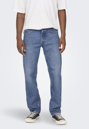 Light blue denim jeans with a straight cut, visible stitching, and five pockets, paired with black sneakers and a white t-shirt.