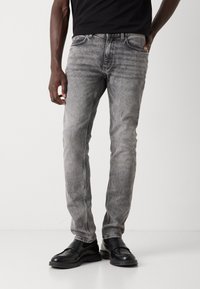 Vaqueros de mezclilla gris con un lavado desvanecido, cinco bolsillos y costuras en contraste. Usados con zapatos de cuero negros y una camiseta negra ajustada.