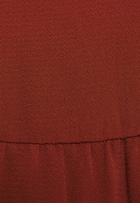 Tissu rouge texturé avec un léger éclat, présentant une couture froncée et des plis, mettant en avant un design à la fois doux et structuré.