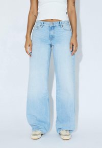 Light blue wide-leg jeans made from denim, featuring a mid-rise waist, five pockets, and subtle fading. Paired with light-colored sneakers.