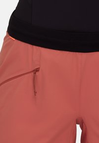 Różowe spodenki sportowe z czarnym paskiem w talii, z boczną kieszenią na zamek błyskawiczny i gładką teksturą. Udekorowane małym pomarańczowym detalem.