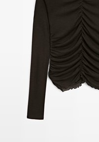 Maglia a maniche lunghe marrone scuro con dettagli arricciati sul davanti e orlo scalloppato. Realizzata in tessuto morbido e elastico.