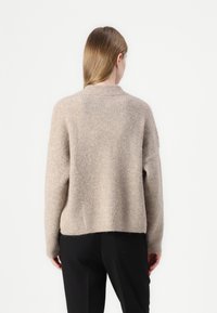 Beige kötött pulóver laza illeszkedéssel, kerek nyakkivágással és bordázott textúrával. Jellemzői közé tartozik a süllyesztett váll és a magas-alacsony szegély kialakítás.