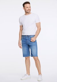 Vaaleansiniset farkkushortsit suoran leikkauksen kanssa, etutaskut ja perinteinen napitus. Yhdistettynä valkoiseen lyhythihaiseen T-paitaan ja valkoisiin lenkkareihin.