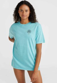 Camiseta de algodón azul claro de manga corta, con un gráfico de una palmera en el lado izquierdo del pecho en negro y amarillo. Textura suave, ajuste casual.
