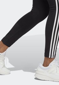 Svarta träningsleggings med vita randiga sidor, slät textur; matchas med vita sneakers med nät- och vadderad design.