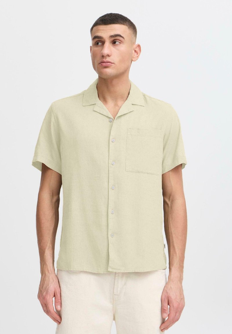 Chemise à manches courtes en lin vert clair avec une seule poche poitrine, fermeture à cinq boutons et coupe décontractée. Texture de tissu lisse.