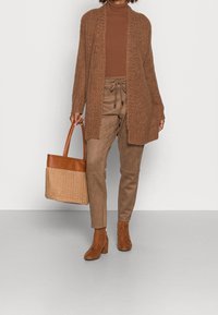 Brun stickad cardigan, figurnära brun polotröja, bruna mocka tapered byxor, bruna klackade ankelskor och en ljusbrun vävd tote-väska.