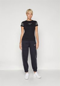 Juoda sportinė marškinėliai su trumpomis dryžuotomis rankovėmis, logotipas ant krūtinės; derinami su juodomis sportinėmis kelnėmis, kuriose baltos šoninės juostos ir apkaustai.