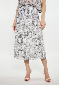 Witte midi rok met zwart bloemenpatroon, lichtgewicht stof, A-lijn vorm en elastische tailleband. Gecombineerd met witte hoge hakken.
