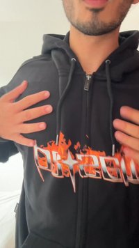 Sudadera con cremallera negra que presenta un prominente diseño de llamas blancas y naranjas con el texto "DR200" en el pecho. Tejido texturizado y capucha con cordón.