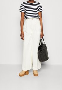 Stribede navy og hvide kortærmede t-shirt, hvide brede bukser, beige platform-sandaler og en sort vævet tote bag.