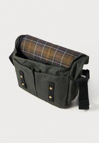 Zöld vászon üzenetküldő táska, kockás mintájú fedéllel, arany hardware-rel és két elülső zsebbel. Állítható fekete pánt a hordozásához.