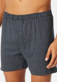 Navy striippiset boxerit pehmeästä kankaasta, joissa on ohuita valkoisia raitoja, joustovyötärö ja pieni nappisulku edessä.