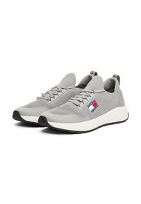 Sneaker in maglia grigia con punta arrotondata, lacci, patch del logo in rosso, bianco e blu, e una suola intermedia bianca con suola in gomma nera.