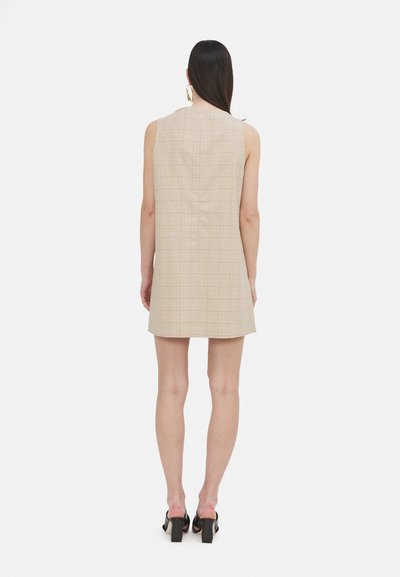 Beiges ärmelloses Kleid mit kariertem Muster, geradem Schnitt und Schlitzen im Rücken. Kombiniert mit klobigen schwarzen High Heels.