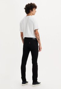 Melni pieguļoši džinsa džinsi ar kabatām aizmugurē un logotipa plāksteri. Kombinēti ar baltu īsroku T-kreklu un melnām kedām.