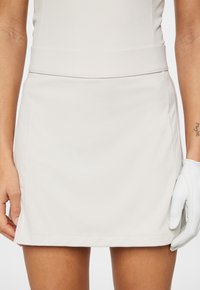 Ljus beige golfkjol med en slät textur, elastisk midja och sidofickor. Har rena linjer och en rak skärning vid nederkanten.