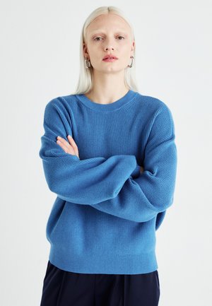 Blå strikket genser med rund hals, ribbet tekstur og senkede skuldre, med lange ermer og en avslappet passform.