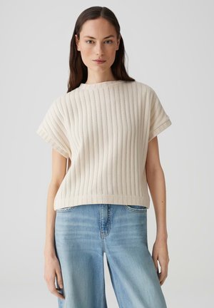 Korte mouwen, ribbeltop in lichtbeige, met een hoge halslijn en een ontspannen pasvorm, gecombineerd met lichtblauwe wijde jeans.