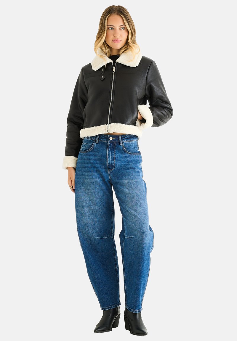 Black leather cropped jacket with cream shearling collar and cuffs, paired with high-waisted blue denim jeans and black ankle boots.
