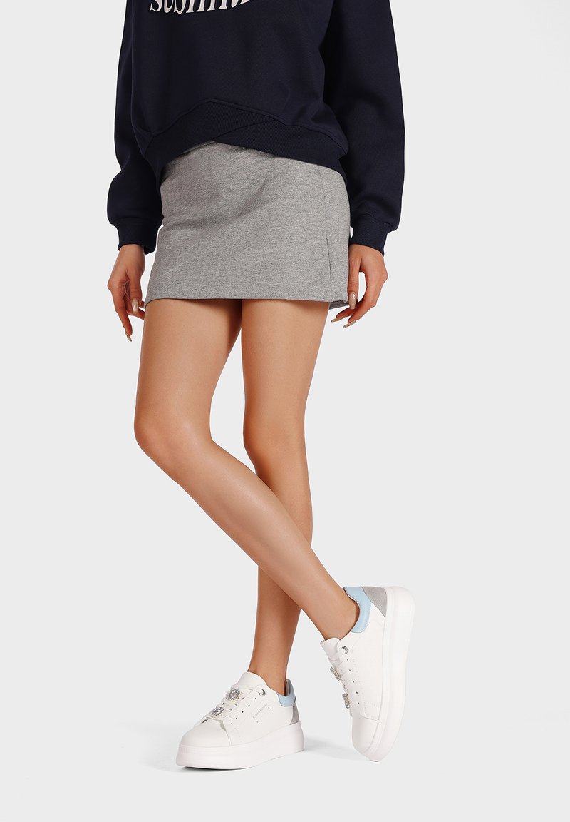 Mini gonna grigia, felpa blu marina con testo "sushimi" e sneakers bianche con accenti blu e decorazioni in metallo. Texture del tessuto liscia.