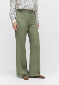 Wijde broek in licht olijfgroene stof, met een gladde textuur en zijzakken, gecombineerd met een blouse met bloemenpatroon.