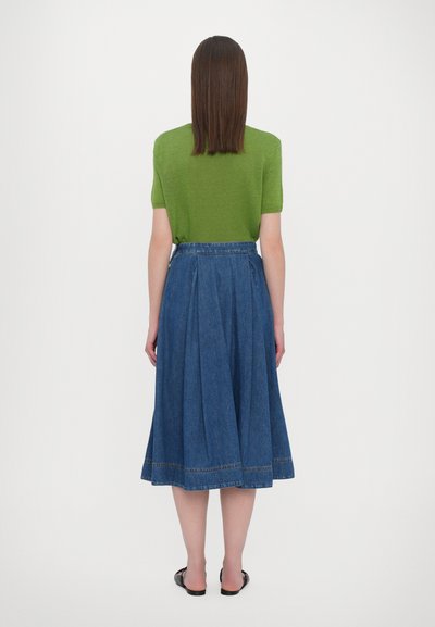 Groene kortdurige trui met korte mouwen, gecombineerd met een lange, uitlopende spijkerrok. De rok heeft een geplooide taille en zichtbare stiksel langs de zoom.