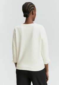 Maglione bianco con texture, maniche a tre quarti e dettagli legati ai polsi. Finitura liscia, dettagli nelle cuciture laterali e scollatura rotonda.