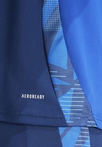 Tissu athlétique bleu avec un motif géométrique, texture lisse et marque "AEROREADY" en blanc. Plusieurs nuances de bleu sont présentes.