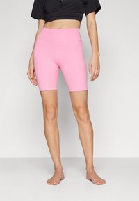 Różowe rowerowe szorty o wysokim stanie, wykonane z elastycznego materiału, z gładką fakturą i długością do kolan, w połączeniu z czarną, krótką bluzką.