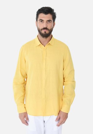 Camicia gialla in lino con bottoni, maniche lunghe e colletto classico, caratterizzata da una vestibilità comoda e una stoffa leggermente testurizzata, abbinata a pantaloni bianchi.