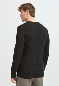 Dunkler, texturierter Strickpullover mit langen Ärmeln und Rundhalsausschnitt, der ein geripptes Muster und einen leicht verlängerten hinteren Saum aufweist.