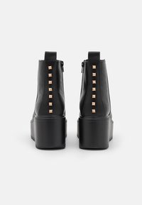 Stivaletti neri in ecopelle con suola platform, caratterizzati da una fila di borchie color oro sul retro e una chiusura con zip sul lato.
